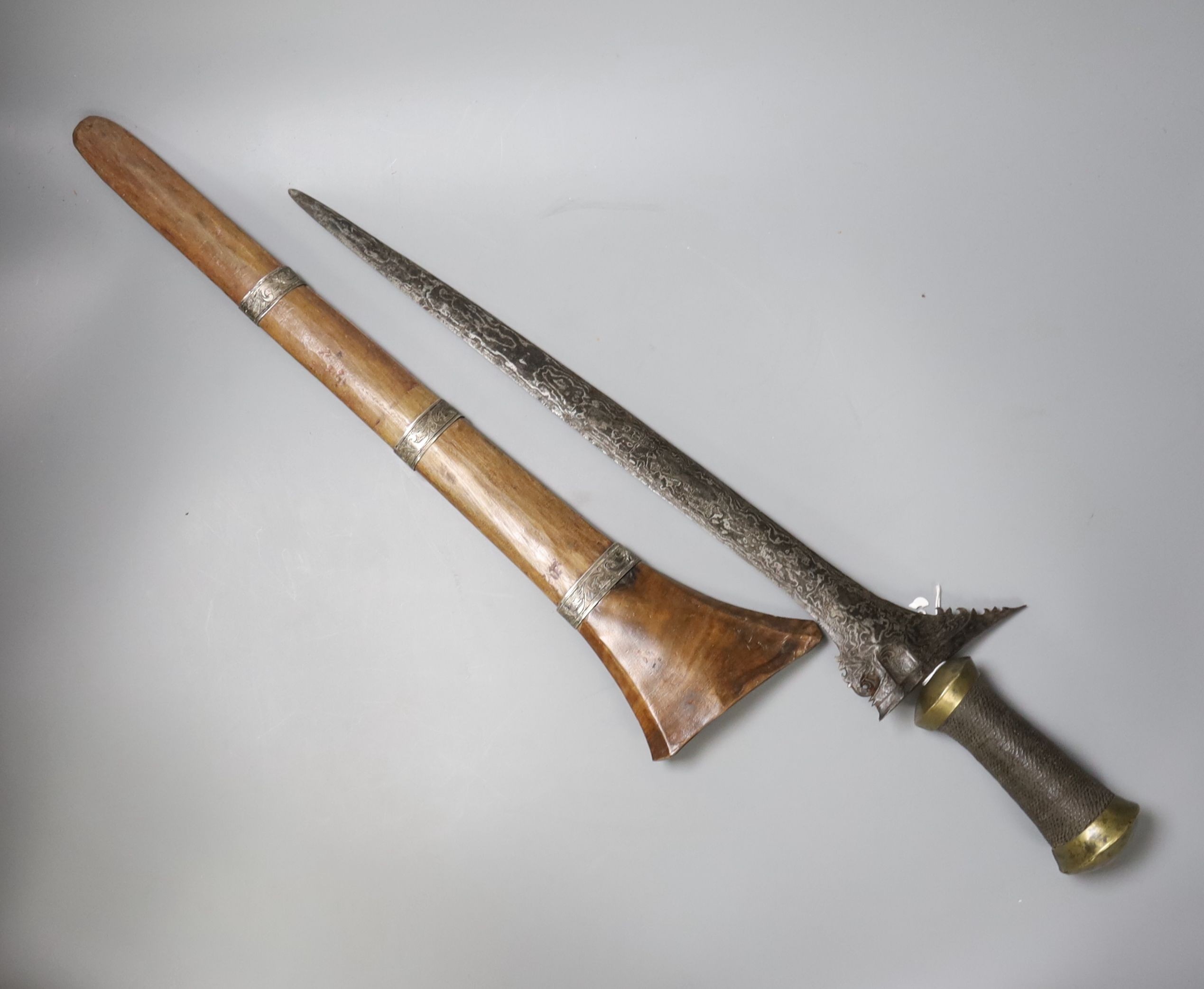 An Indonesian dagger kris, 19th century, earlier broad black and silver-coloured watered blade, brass mounted handle wound with woven hair, wooden scabbard with engraved silver mounts, blade 43.5cms